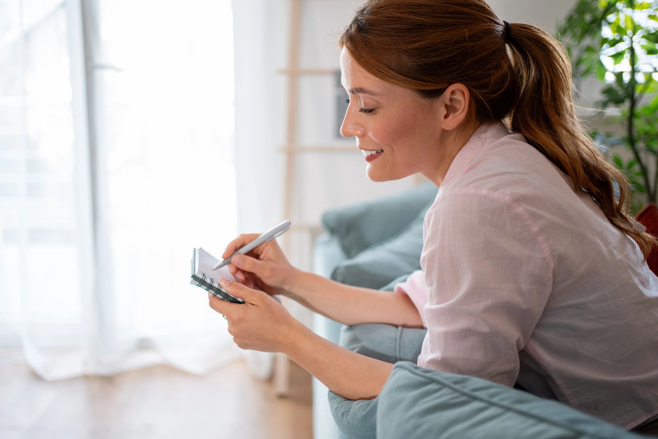 Woman writing in a notebook on a sofa
